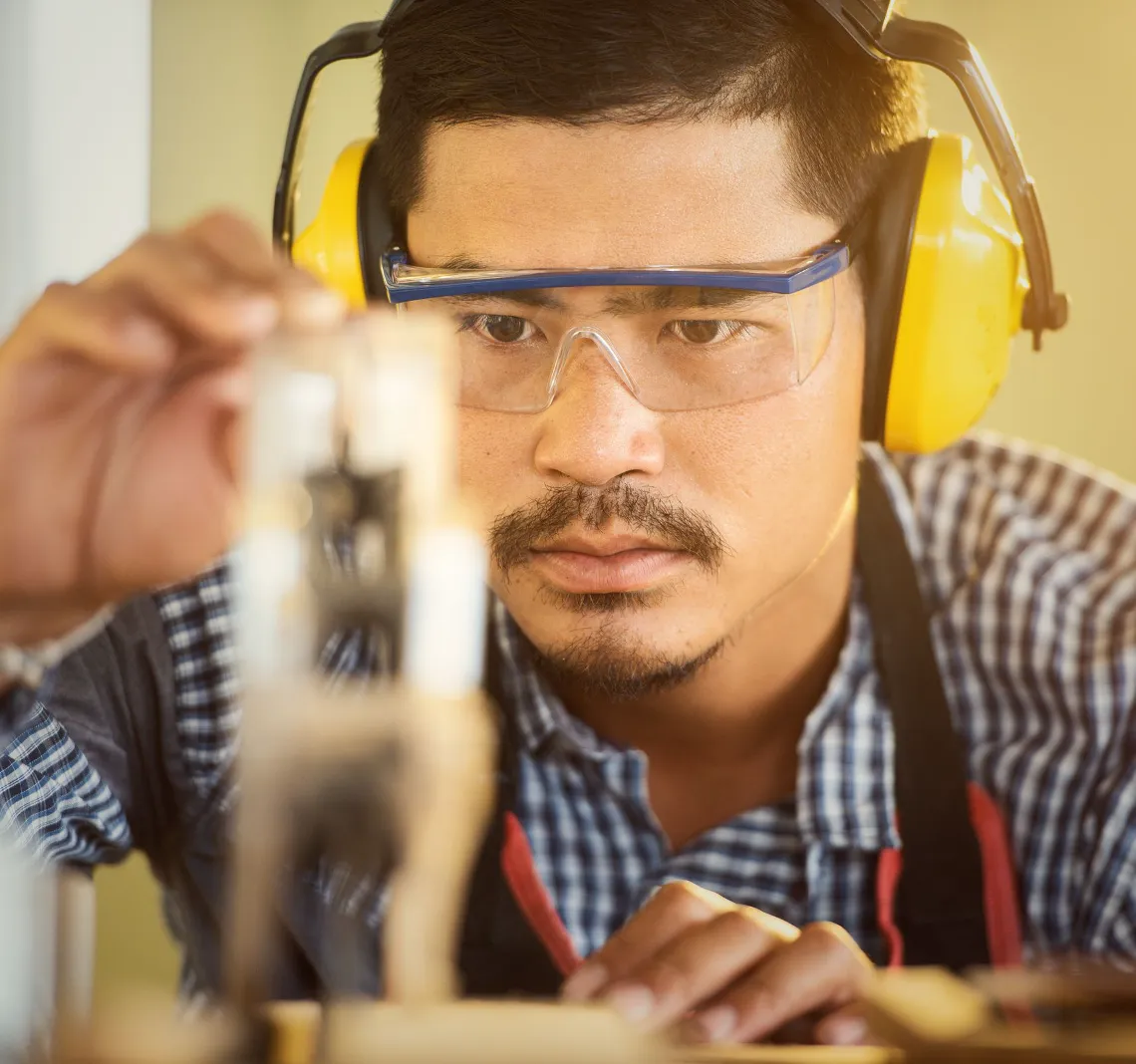 A carpenter in ear defenders checking a cut